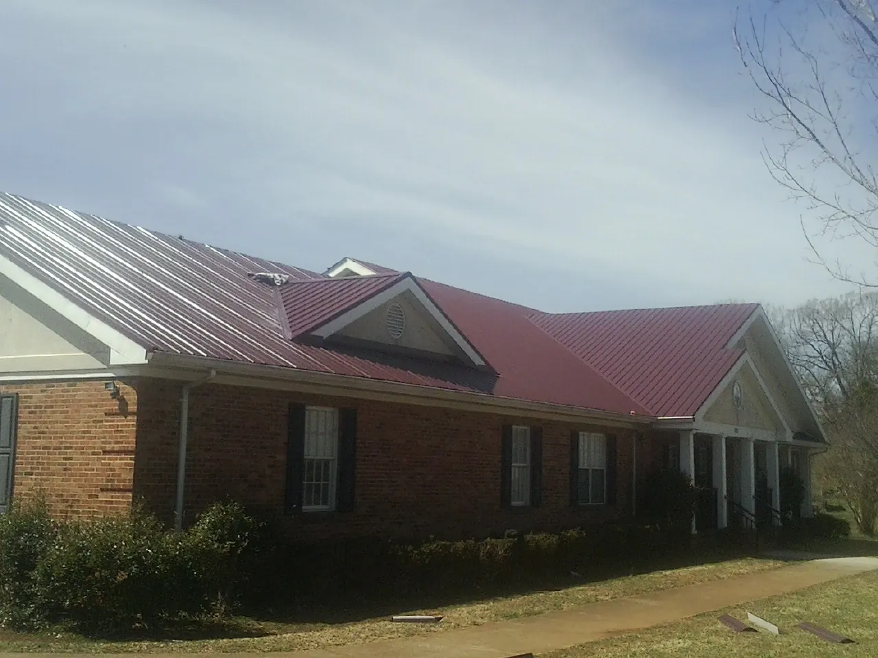 Red metal roof with gabled entries on a long brick building, from a Hail Damage Roof Repair job in Wytheville