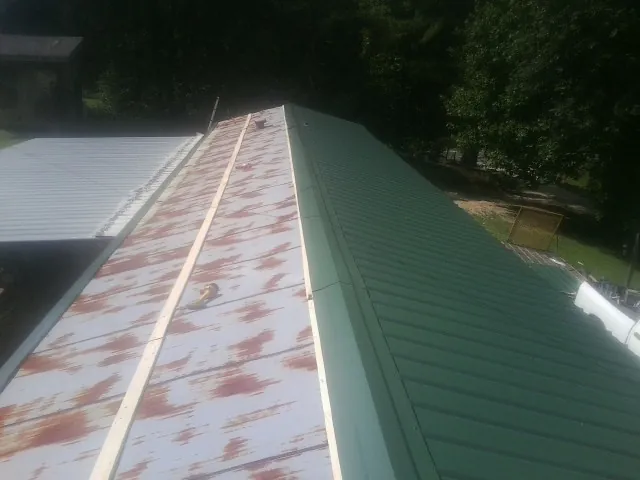 Old rusted panels beside newly installed green metal roofing — Wind Damage Roof Repair by Roofing Brothers in Wytheville