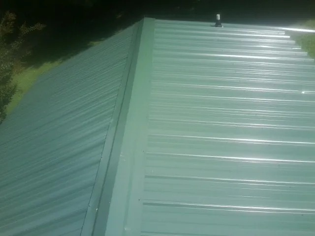 New green metal panels meeting at the ridge of a roof — Flat Roof Repair work by our crew in Wytheville