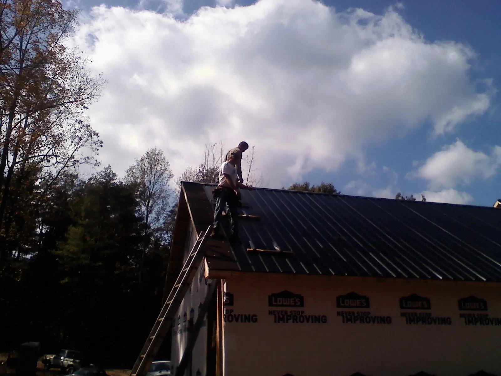 Roofer fastening dark metal panels high against a cloudy sky, from a Roof Inspection job in Wytheville