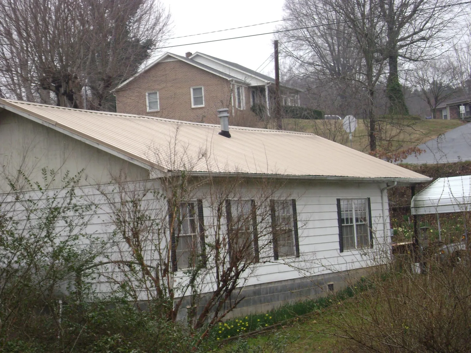 Tan metal roof on a white sided house set into a hillside — Commercial Roofing by Roofing Brothers in Wytheville